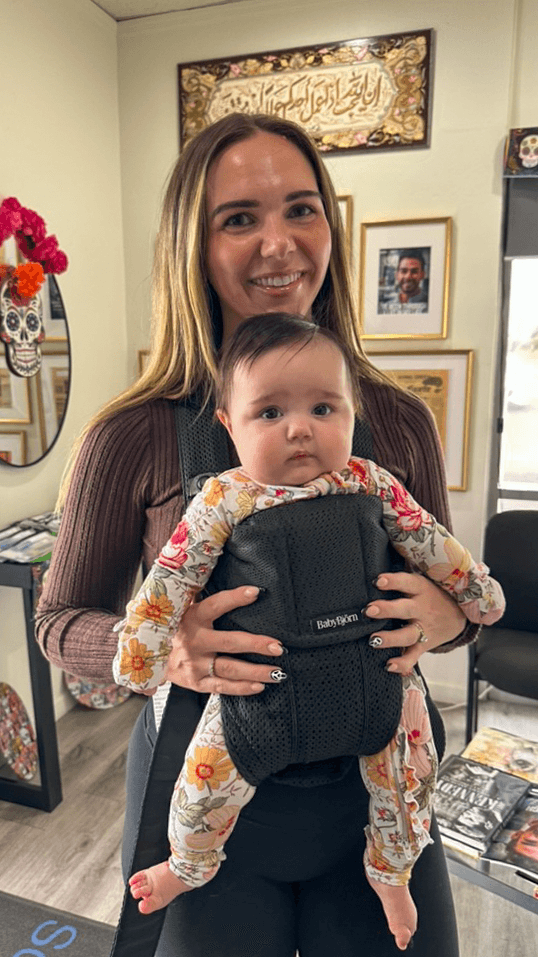 A smiling adult holds a baby in a carrier inside the Southern Smiles office.