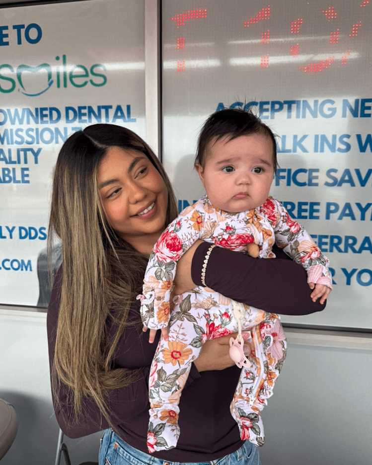 An adult smiles while holding a baby outside the Southern Smiles office.