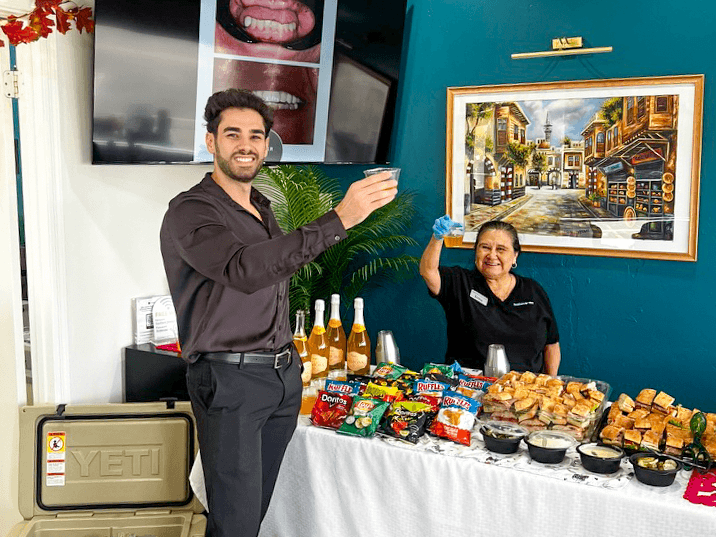 Two members of the Southern Smiles team raise their drinks beside a table of refreshments inside the office.