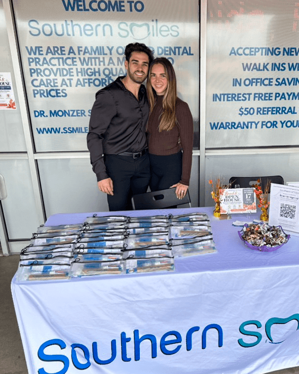 Two smiling adults stand behind the dental-care giveaway table outside Southern Smiles.